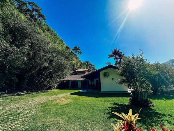 A house with a tiled roof, surrounded by a well-maintained lawn and dense trees.