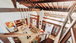 A spacious interior with a high ceiling, wooden beams, a staircase, and a seating area with a sofa and chairs. - Casa Rio Habitat (Petrópolis)