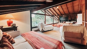 A cozy room with a bed, a chair, a table, and a TV. - Casa Rio Habitat (Petrópolis)