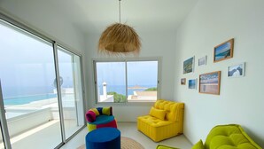 A modern living room with large windows, a view of the sea, and colorful furniture. - Horizon Marin in Raf Raf (Raf Raf)