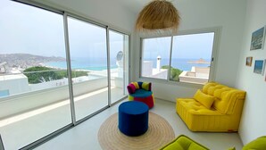 A modern living room with large windows, a yellow sofa, a colorful chair, and a hanging light fixture. - Horizon Marin in Raf Raf (Raf Raf)