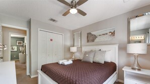 Un dormitorio con cama, lámparas de noche, ventilador de techo, cómoda y espejo.