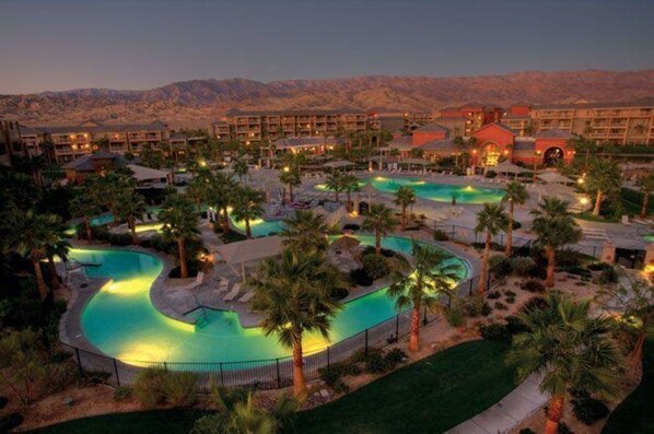 Surrounded by palm trees and mountains, this resort offers multiple pools and a hotel with a distinctive red-roofed building.
