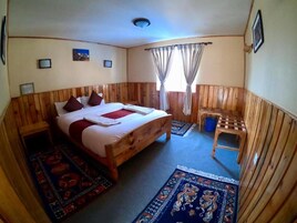 Una habitación con paneles de madera, una cama, una mesita y dos alfombras.