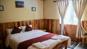 A bedroom with a wooden headboard, a bed with white bedding and red accents, a window with curtains, and a small bedside table. - Panorama Lodge and Restaurant  (Namche Bazar)