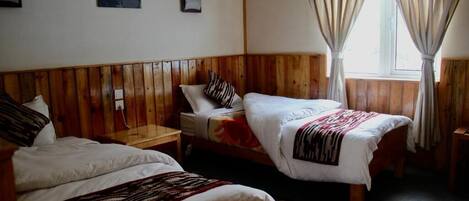 Una habitación con dos camas individuales, paneles de madera, un ventanal con cortinas y una mesita de noche pequeña.