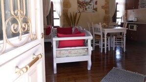 Un comedor con una mesa y sillas blancas, un sofá con cojines rojos y un cuadro en la pared.