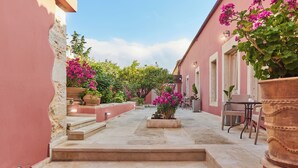 Un patio con escalones que conducen a una zona de estar, rodeado de muros rosados y plantas en macetas.