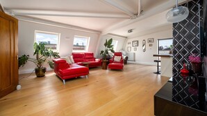 A spacious living room with a red sofa set, wooden flooring, and large windows offering a view of the cityscape. - GuestReady - Modern 2BR w Balcony in Poplar (London)