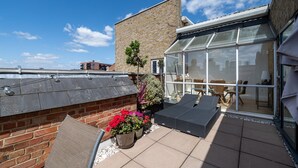 A rooftop terrace with a glass enclosure, a brick wall, and outdoor seating. - GuestReady - Modern 2BR w Balcony in Poplar (London)