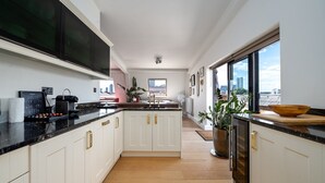 A modern kitchen with white cabinets, a black countertop, and a large window offering a city view. - GuestReady - Modern 2BR w Balcony in Poplar (London)