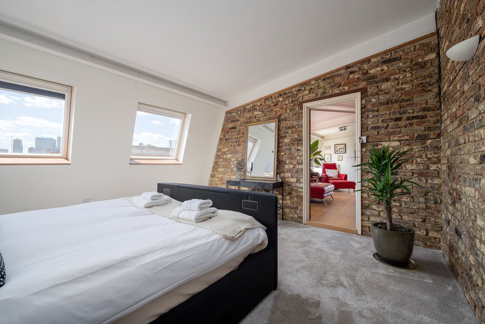 Un dormitorio moderno con una cama grande, un aparador, un espejo y una planta en maceta.