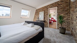 A modern bedroom with a large bed, a dresser, a mirror, and a potted plant. - GuestReady - Modern 2BR w Balcony in Poplar (London)