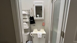 A small bathroom with a toilet, sink, and mirror. There is a towel rack with a towel and a black bag hanging on it. A white rug is on the floor. - Downtown Starkville Apartment! (Starkville)