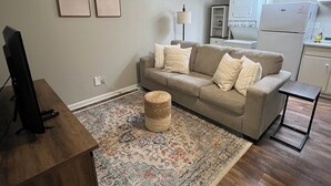 A living room with a sofa, a coffee table, a rug, a television, and a ceiling fan. - Downtown Starkville Apartment! (Starkville)