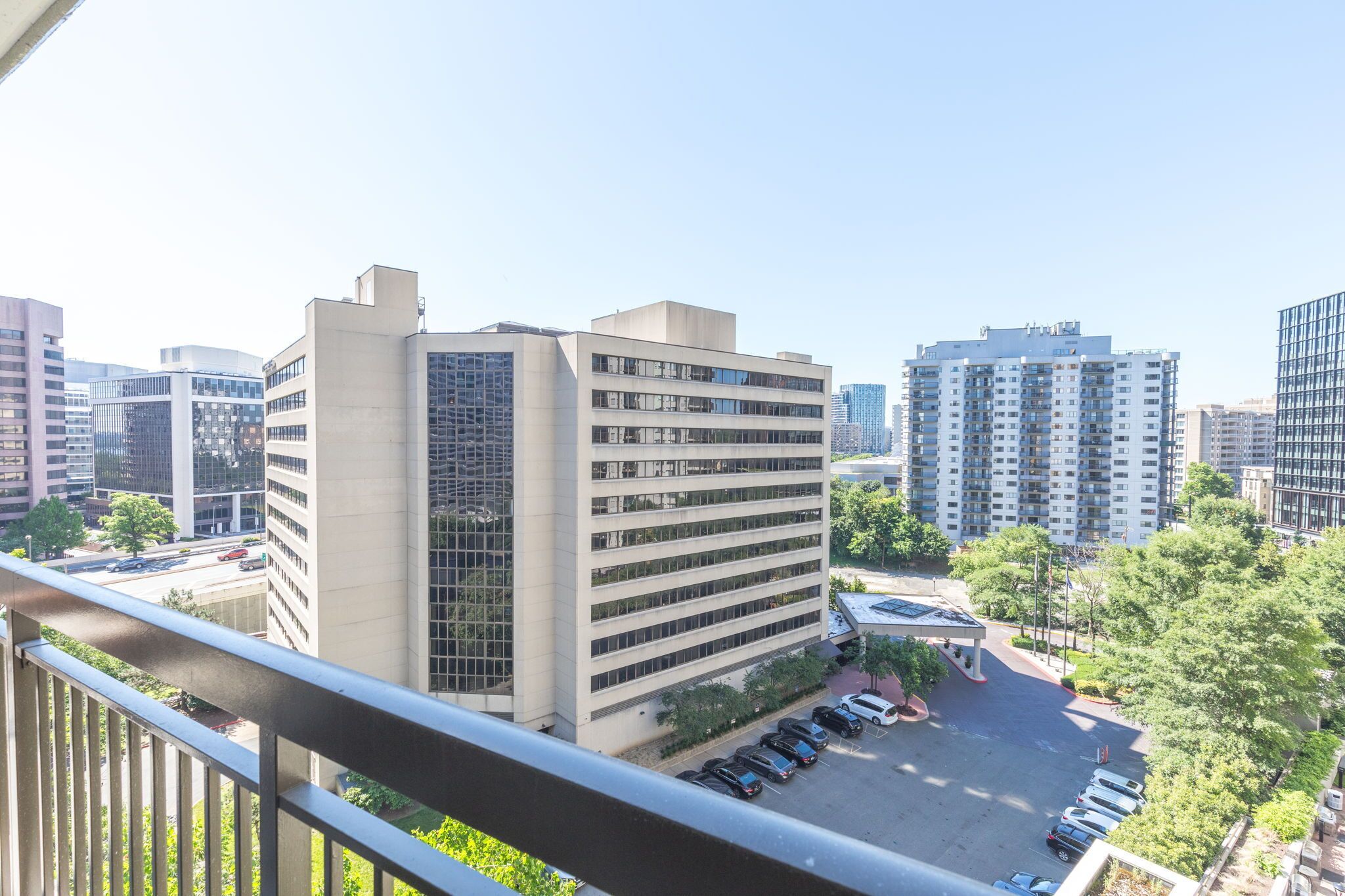 A high-rise building with a modern architectural design, surrounded by other high-rise buildings and a parking area with several cars.