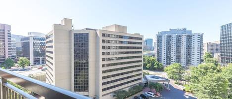 A high-rise building with a modern architectural design, surrounded by other high-rise buildings and a parking area with several cars.