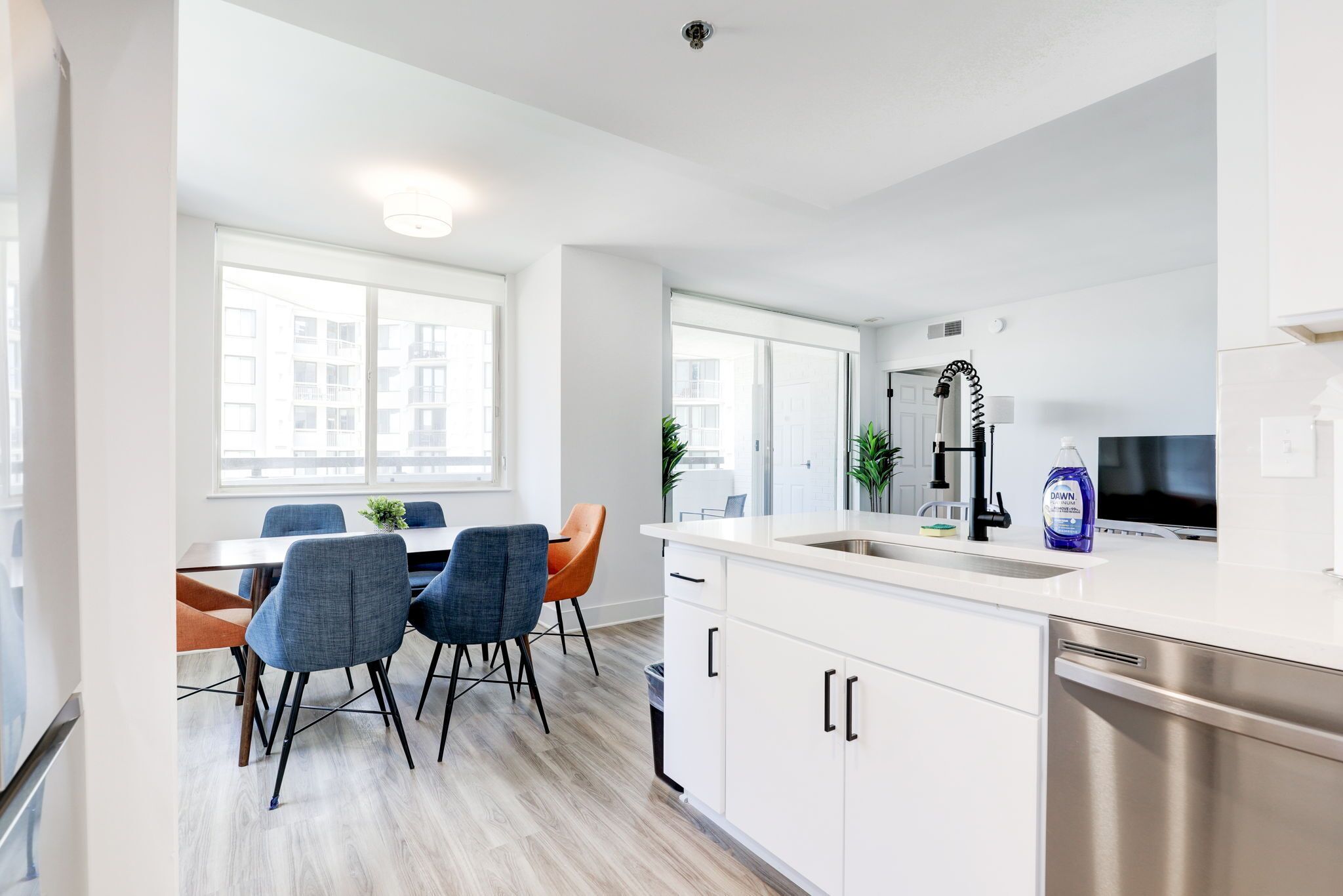 A modern kitchen with white cabinets, a stainless steel dishwasher, and a large window providing natural light.