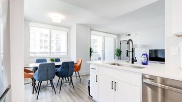 A modern kitchen with white cabinets, a stainless steel dishwasher, and a large window providing natural light.