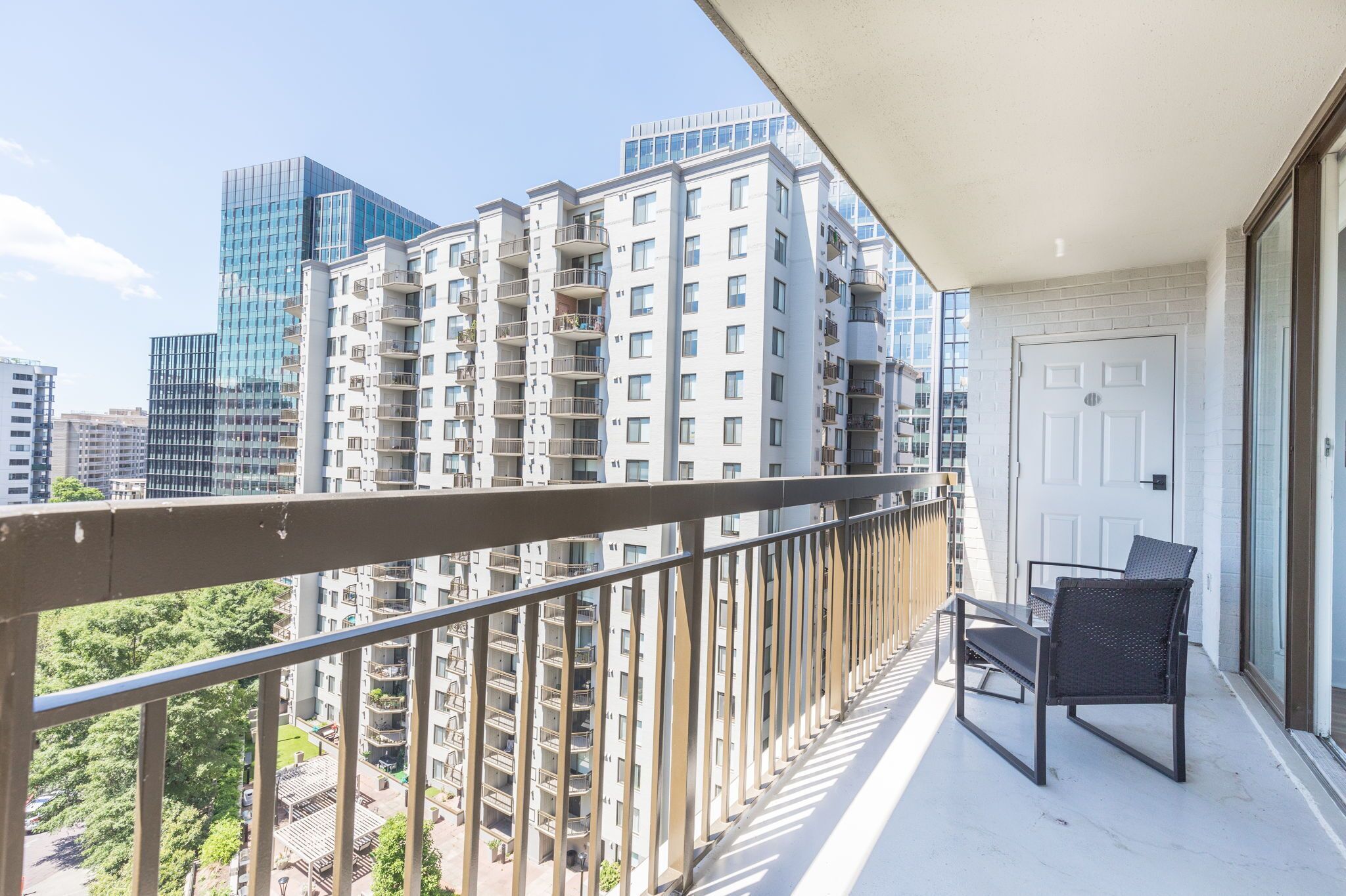 Un balcón con vista a edificios altos, una puerta y una silla.