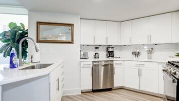 A modern kitchen with white cabinets, stainless steel appliances, and a large window.