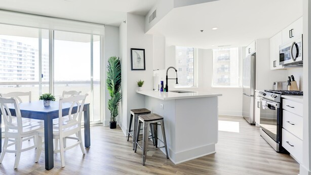Une cuisine moderne dotée d’un îlot central, de meubles blancs et d’une grande fenêtre qui laisse entrer la lumière naturelle.