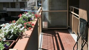 Ein Balkon mit einem Metallgeländer, einem Blumentopf mit Blüten und Blick auf ein mehrgeschossiges Gebäude.