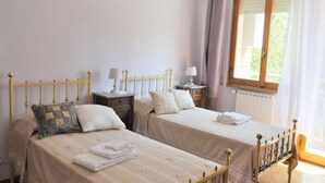 Ein Schlafzimmer mit zwei Einzelbetten, Nachttischen mit Lampen, einem Fenster mit Vorhängen und einem Heizkörper.