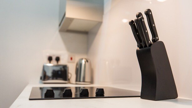Uma cozinha com um conjunto de facas pretas na bancada, uma torradeira e uma chaleira.