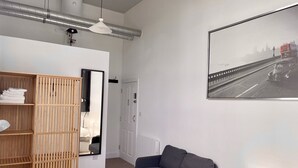 Quarto moderno com sofá cinzento, guarda-roupa de madeira, espelho e fotografia emoldurada de um horizonte urbano na parede.