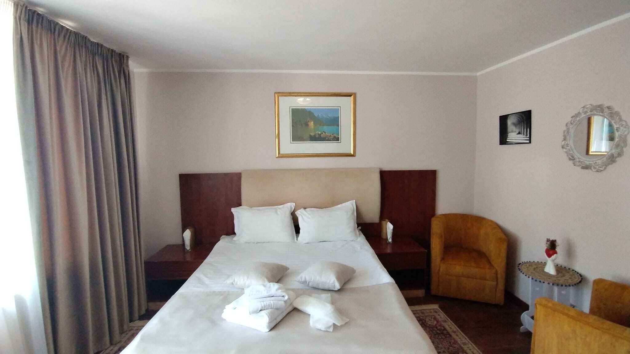 Habitación de hotel con una cama grande, dos mesitas de noche, una silla, una pequeña mesa con un florero y un cuadro enmarcado en la pared.