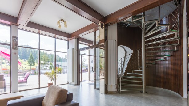 Eine geräumige Lobby mit einer modernen Treppe, großen Fenstern mit Blick ins Freie und einer Sitzecke mit einer Couch.