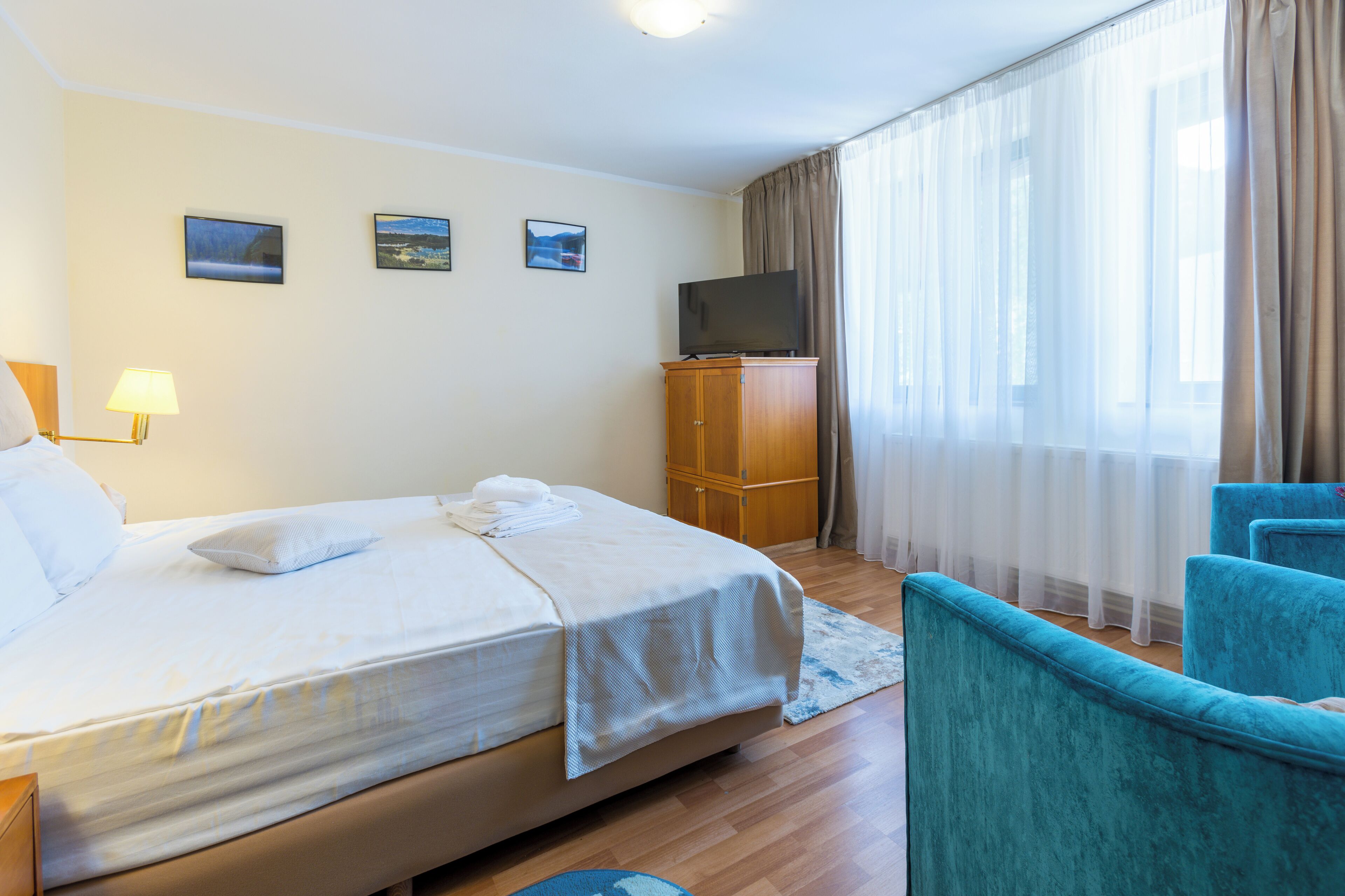 A hotel room with a bed, a television, a wooden cabinet, and a window with curtains.