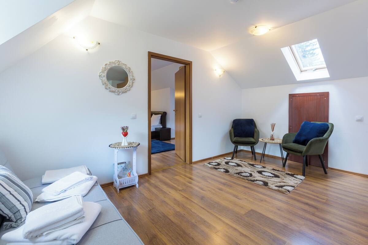 Un salón amplio con piso de madera, un sofá, dos sillones, una mesita y un espejo en la pared.
