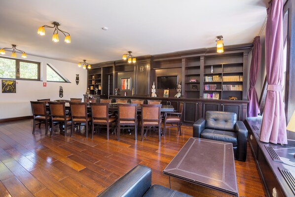 Una habitación amplia con suelo de madera, zona de bar con estanterías y diferentes disposiciones de asientos, incluyendo sillas y un sofá.