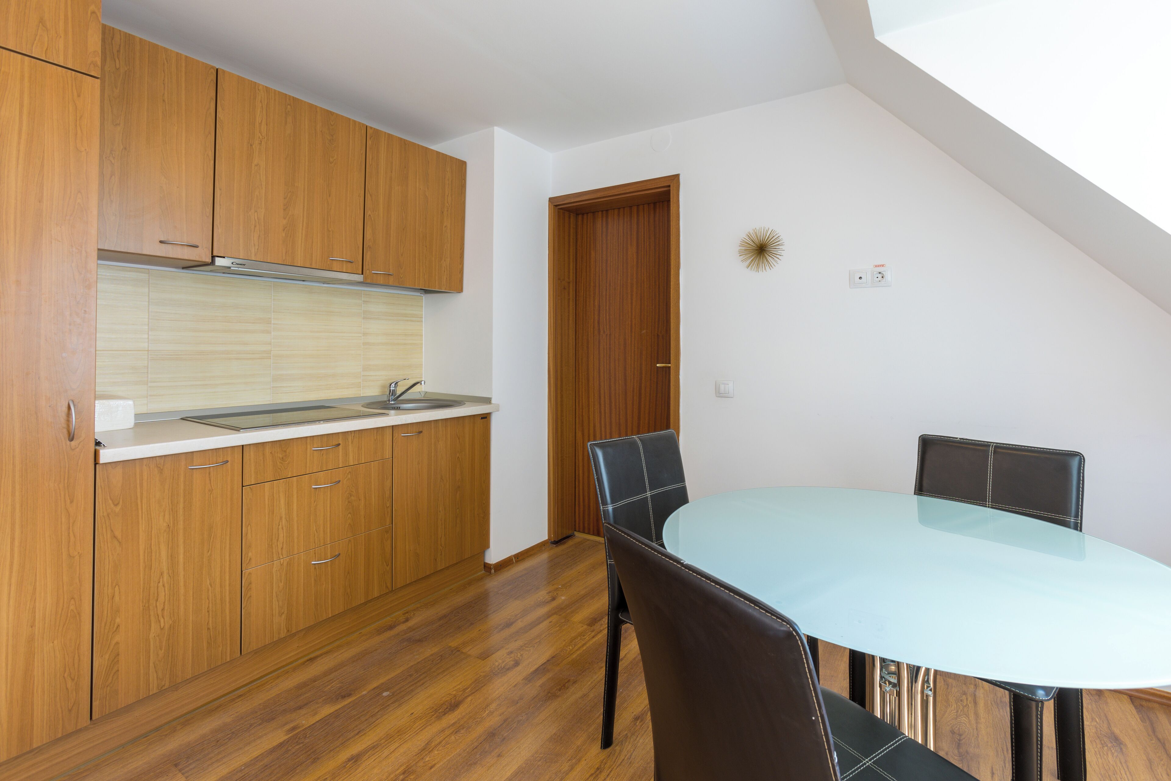 A kitchen with wooden cabinets, a glass table, and a dining area with chairs.