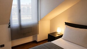 A hotel room with a bed, a nightstand with a lamp, a window with a view of an archway, and a carpet. - 108 APARTMENT (Turin)