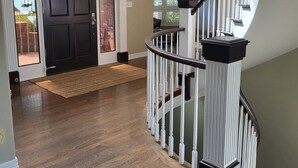 A spacious interior with a wooden floor, a black door, and a white staircase with a black handrail. - Beautiful 5BR home on 1 acre in Highlands Ranch perfect for families (Littleton)
