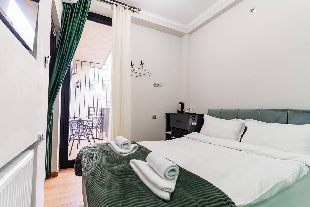 A hotel room with a bed, a nightstand, a chair, and a view of the outside balcony.