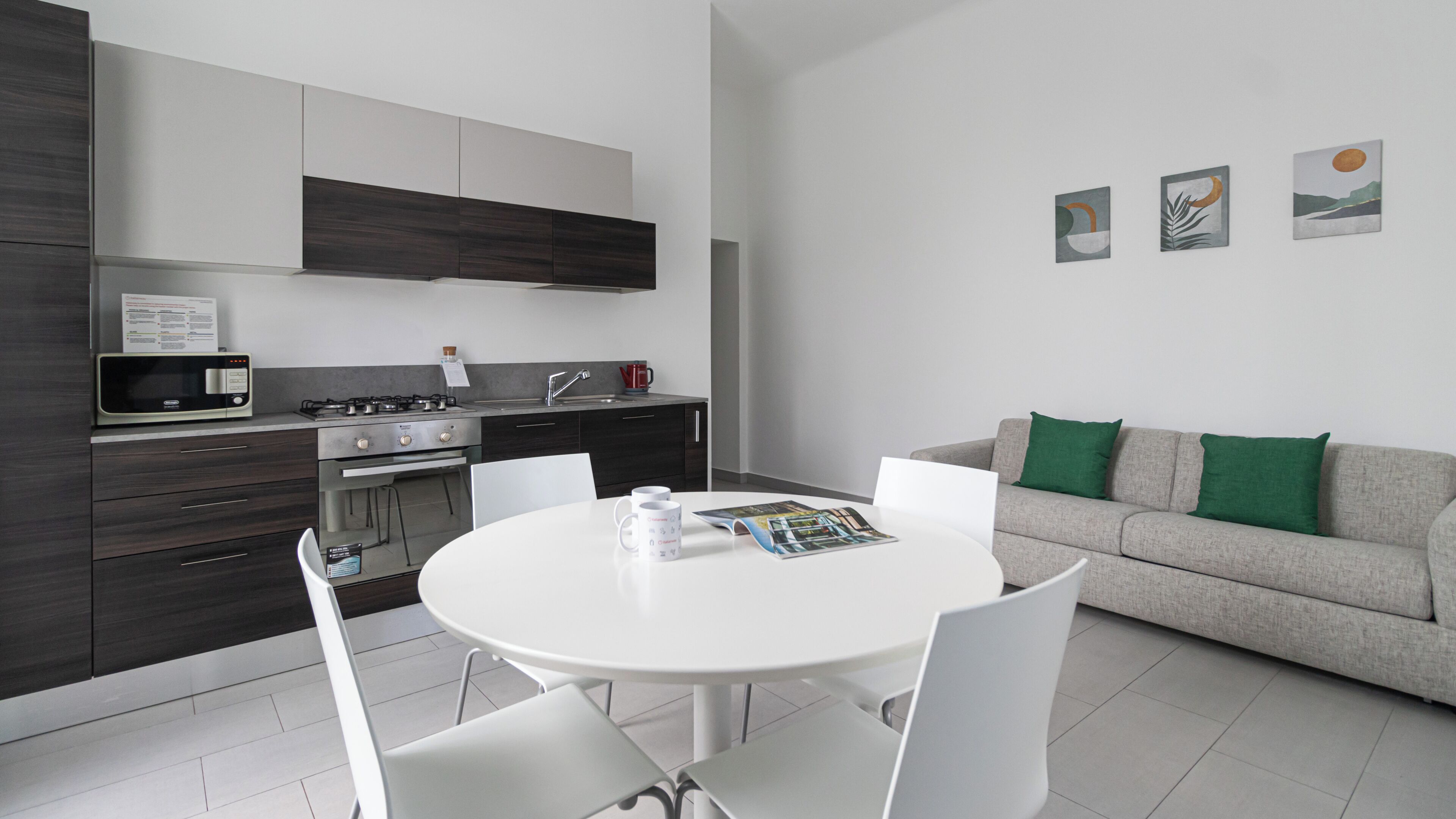 Una cocina moderna con microondas, estufa y horno integrados. Hay una mesa de comedor con sillas y un sofá en la sala.