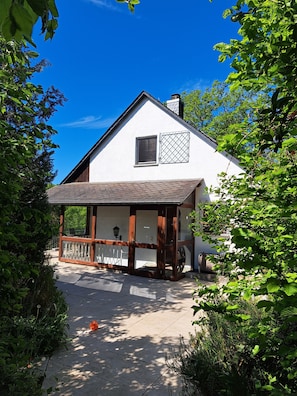 A white building with a wooden porch, a chimney, and a window with a metal grid.