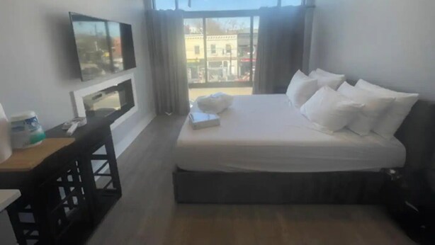 Une chambre d’hôtel avec un lit, un téléviseur fixé au mur, une petite table et une vue sur l’extérieur par une fenêtre.