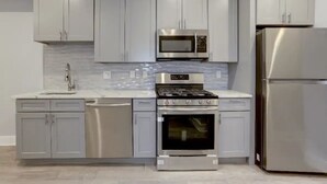 Une cuisine moderne avec des meubles gris, des appareils en acier inoxydable et un dosseret carrelé.