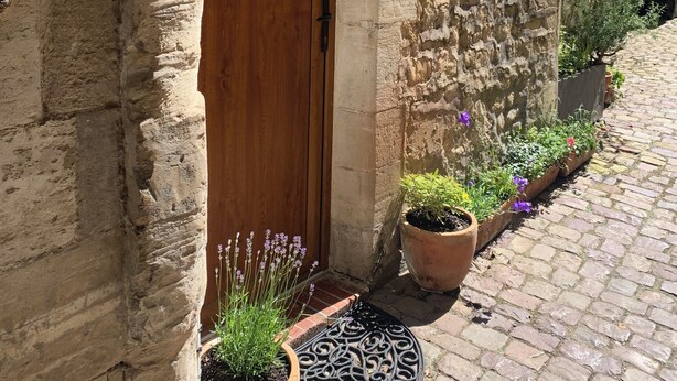 Un edificio in pietra con una porta in legno, con il numero 10, e piante in vasi all'esterno.