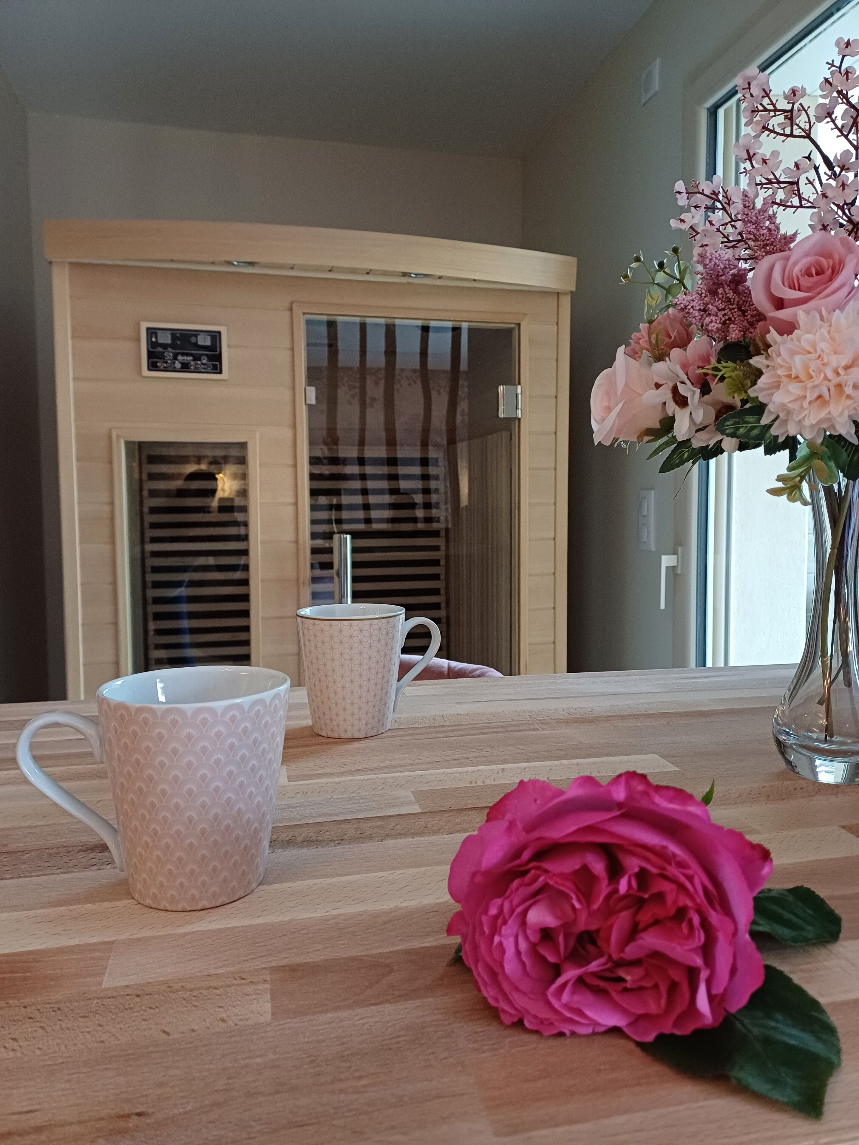 Una mesa de madera con dos tazas decoradas y un florero con flores rosadas.