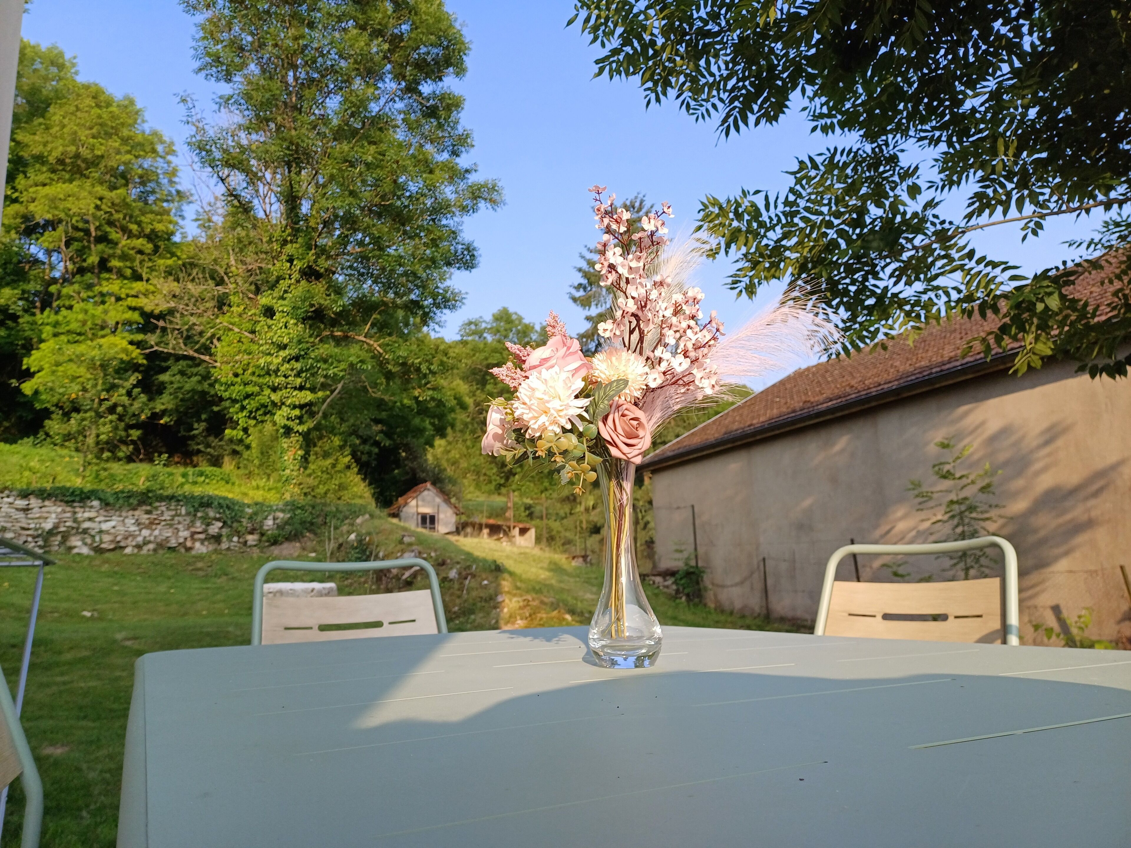 Ein Tisch mit einer Blumenvase in einem Garten.