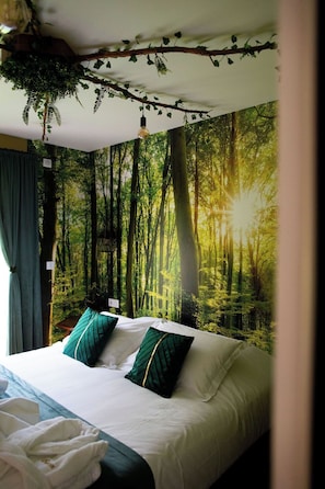 A bedroom with a bed, pillows, and a forest mural on the wall.
