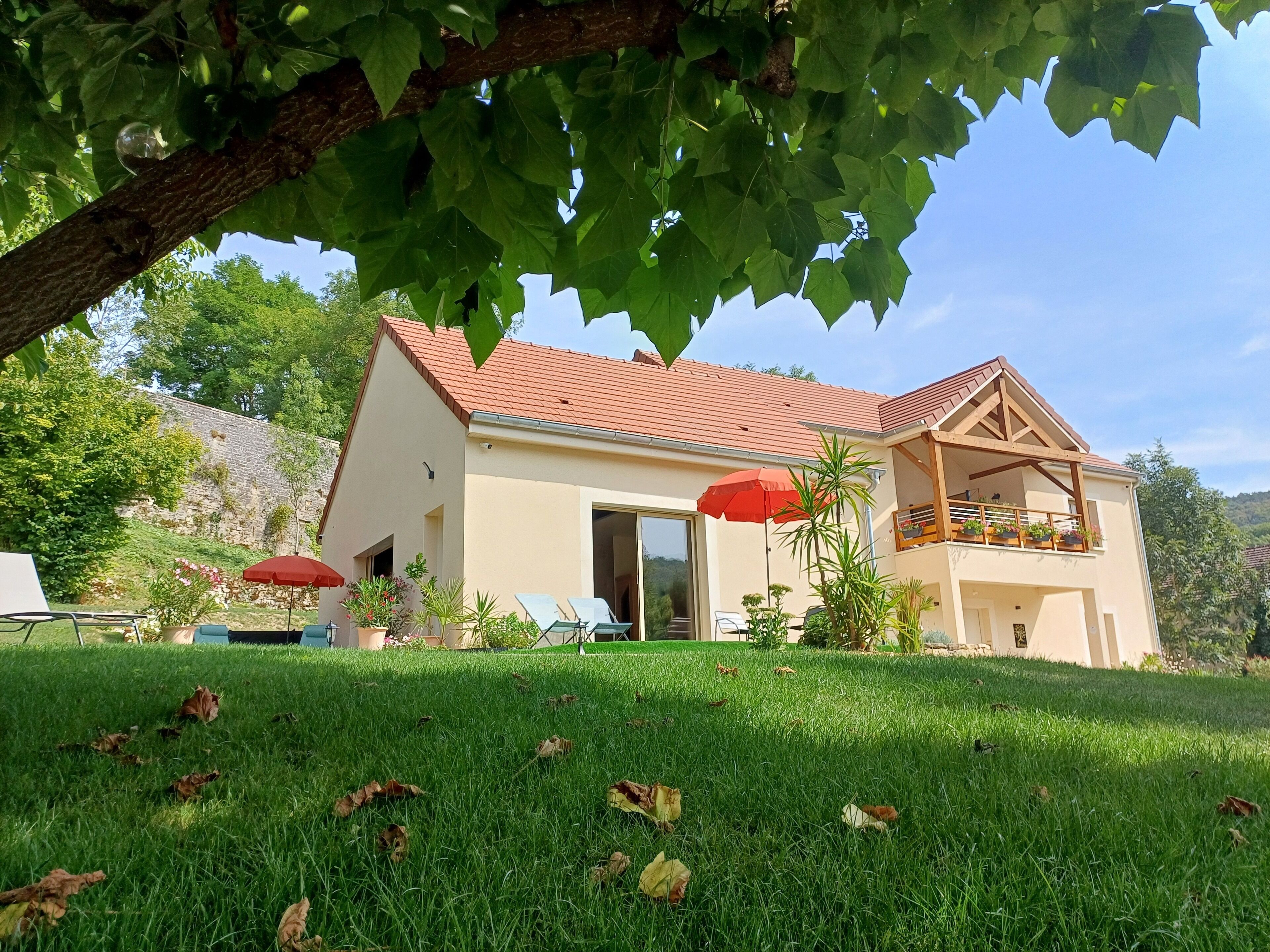 A two-story house with a red-tiled roof, a balcony with potted plants, and a grassy lawn with a few fallen leaves.