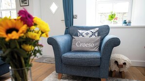 Un fauteuil bleu avec un coussin orné du mot « Croeso », un vase de fleurs et un tabouret en bois.