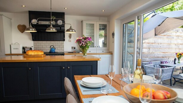 Une cuisine moderne dotée d’un îlot central, d’un coin repas avec une table dressée pour deux personnes et d’une vue sur l’extérieur.
